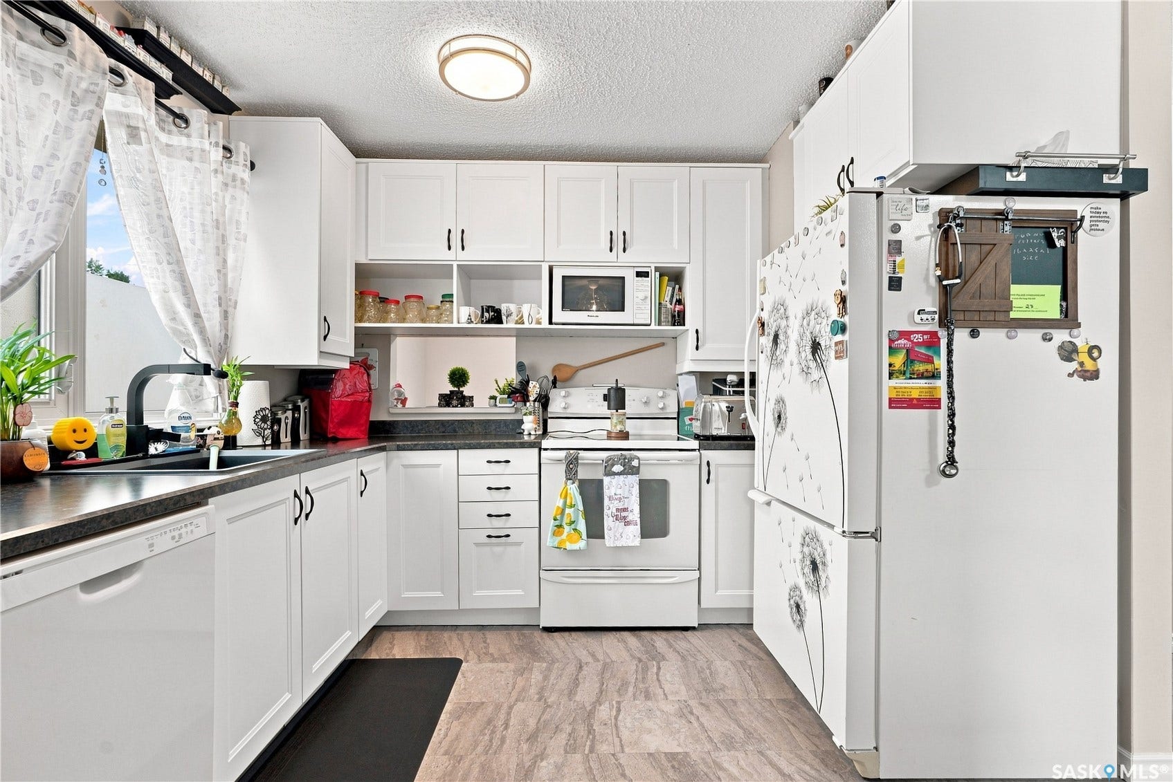 Kitchen featuring white cabinetry, dark countertops, a window over the sink, and light flooring