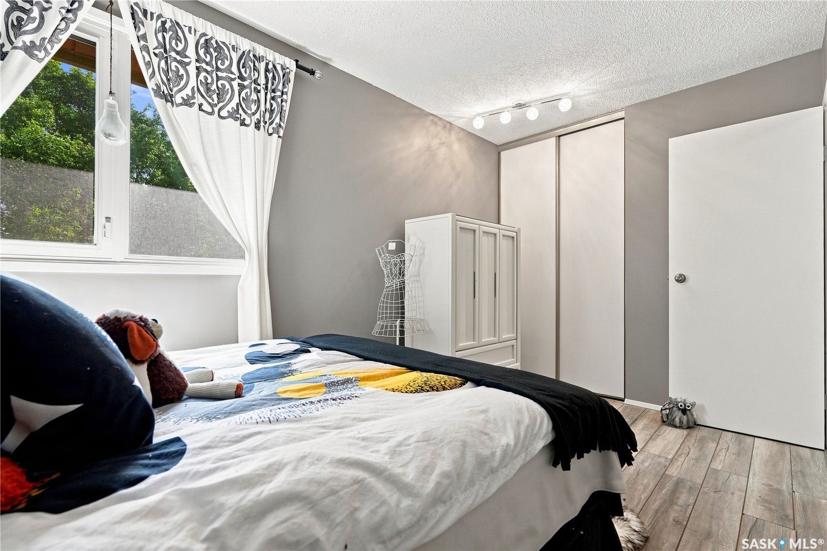Window with white trim, wood-finish flooring, sliding closet doors, and a track lighting fixture
