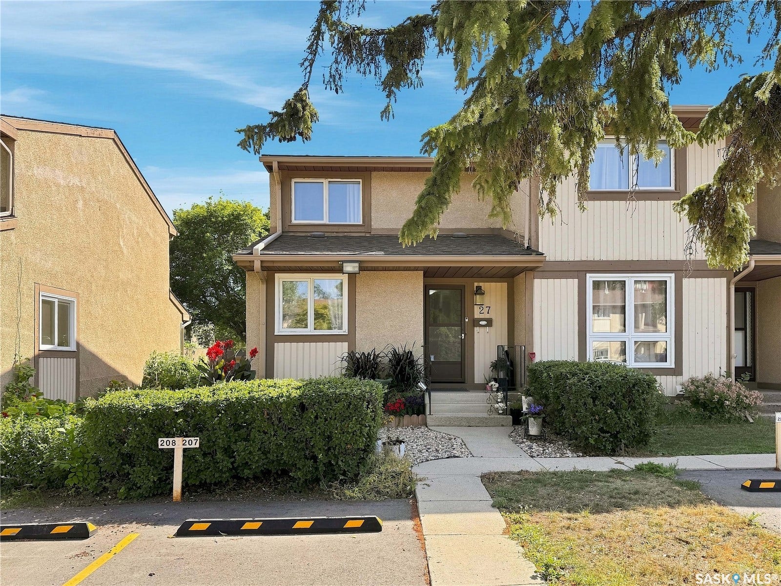 Townhouse home featuring a welcoming front entrance with a covered porch, horizontal siding exterior, and mature landscaping including evergreen trees and manicured hedges