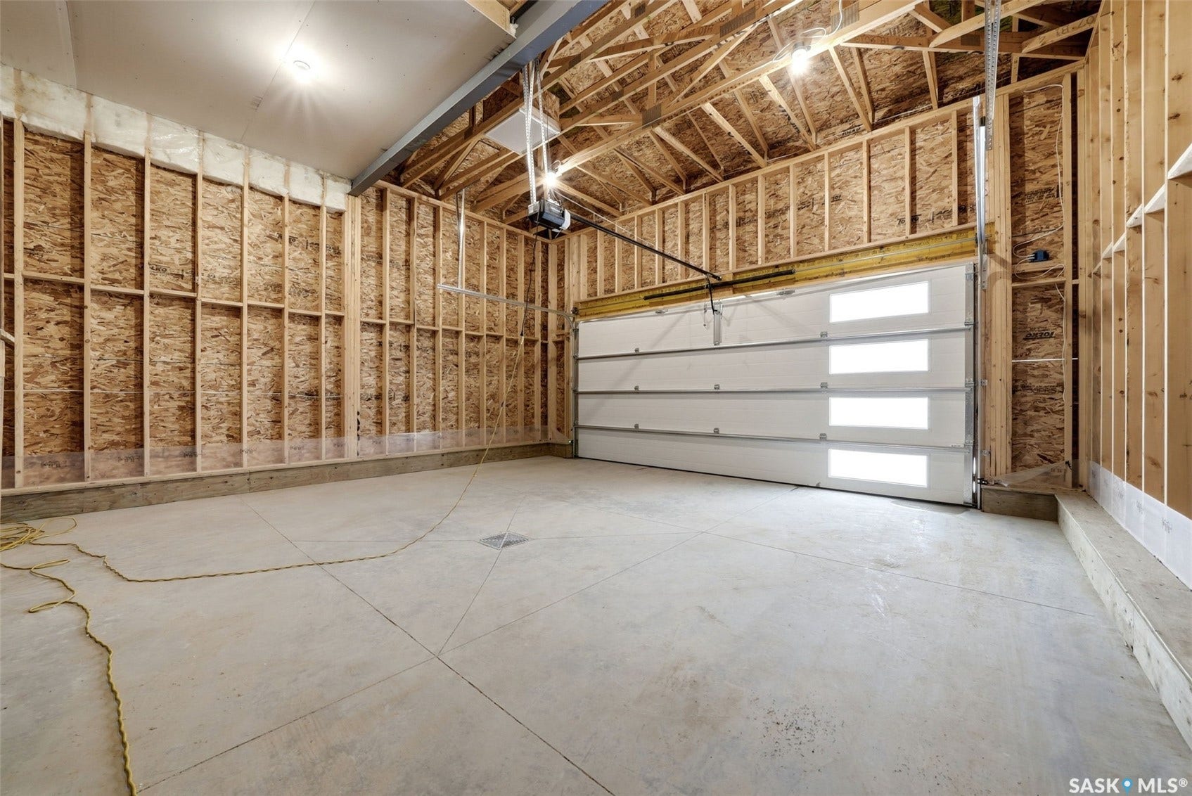 Unfinished garage space featuring a modern sectional garage door with frosted panels, concrete flooring, exposed wood framing, and an automatic garage door opener