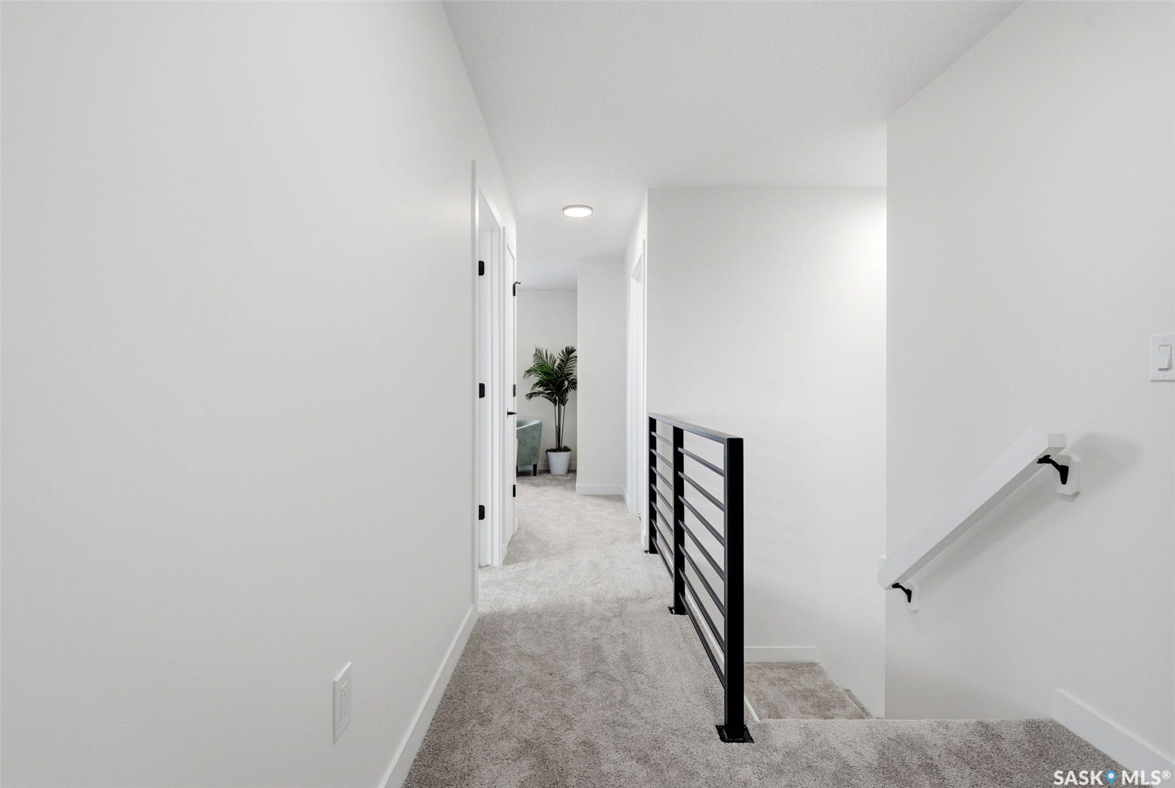 Modern iron baluster railing, white walls, recessed lighting, neutral carpeting, and white trim throughout