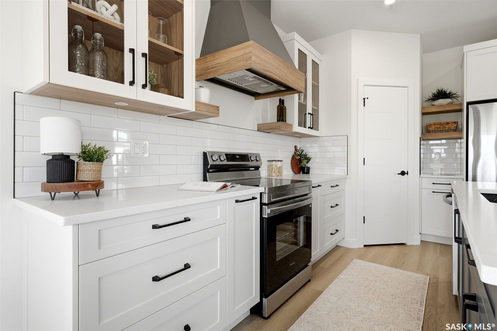 White shaker cabinetry with black hardware, wood-finish flooring, white subway tile backsplash, stainless steel appliances, and white countertops