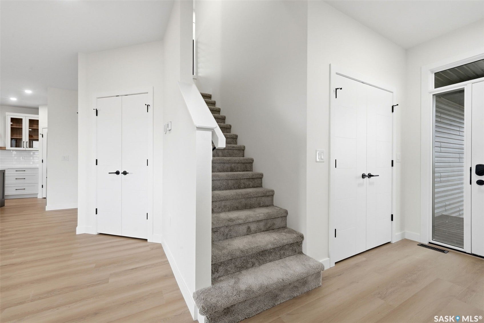 Light wood-finish flooring, carpeted staircase, and white interior doors with matte black hardware