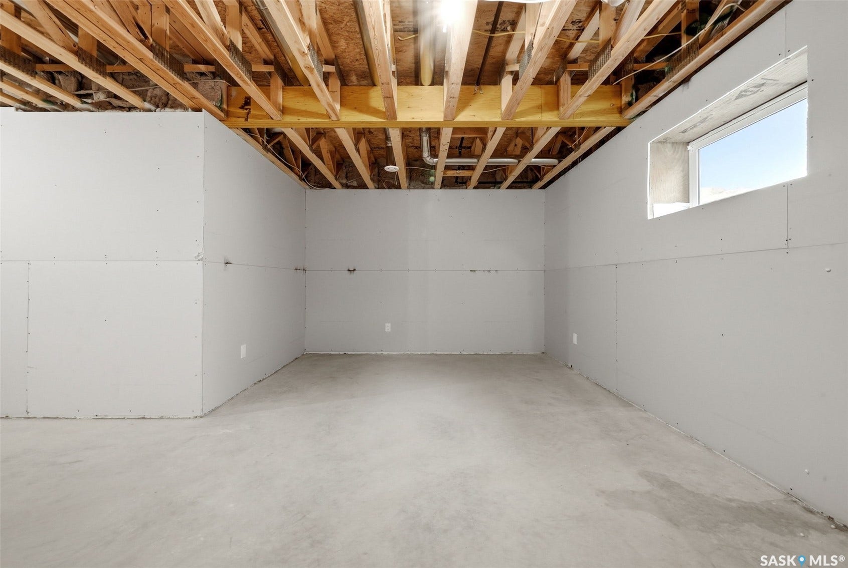 Unfinished basement with exposed ceiling joists, concrete flooring, and prepped drywall