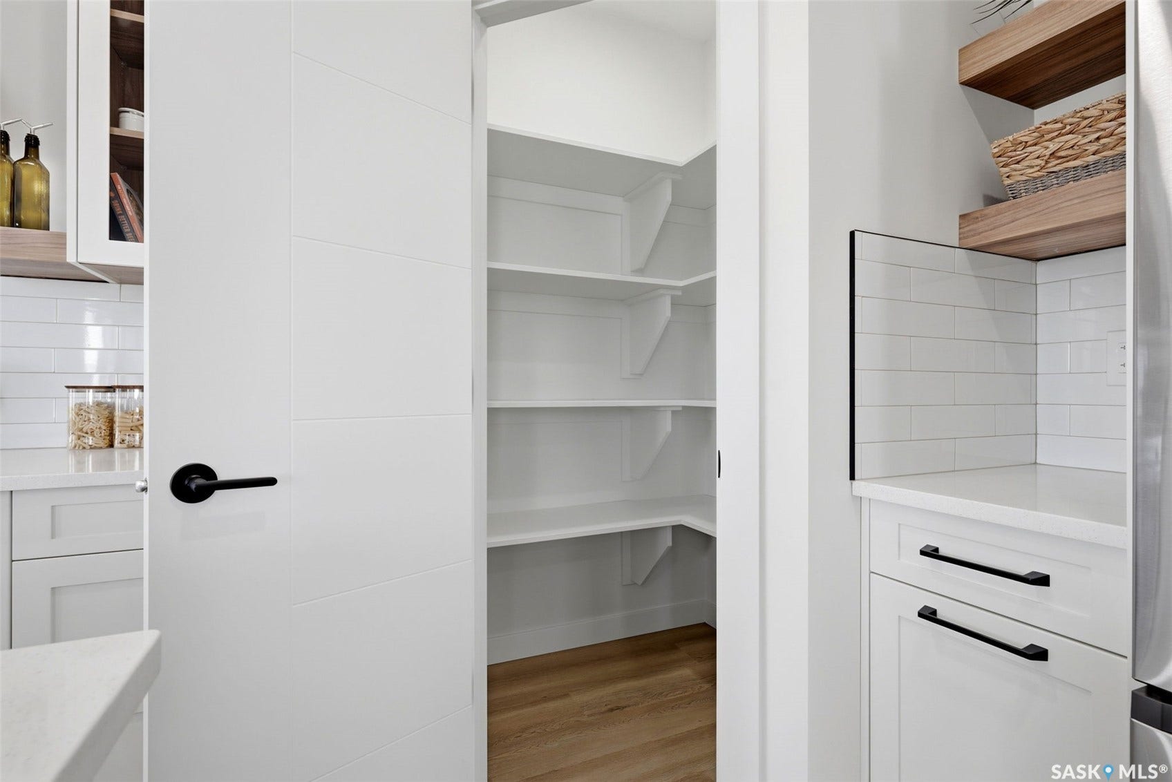 Walk-in pantry with extensive shelving, white flat-panel cabinetry, light wood-finish flooring, and black hardware