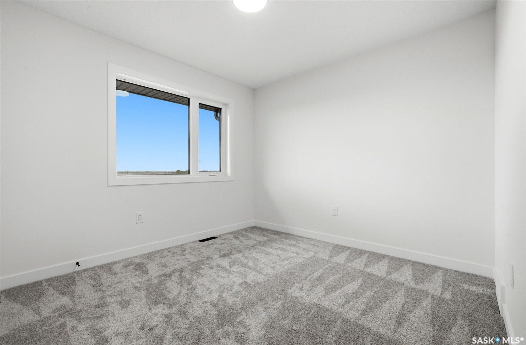 Bright room with a large window, neutral gray patterned carpet, white walls, and a ceiling-mounted light fixture