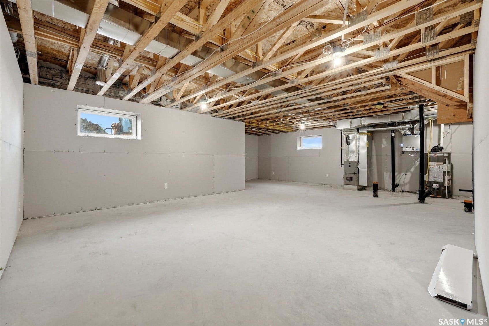 Expansive unfinished basement with exposed wood joists and concrete flooring, featuring multiple egress windows and visible utility systems