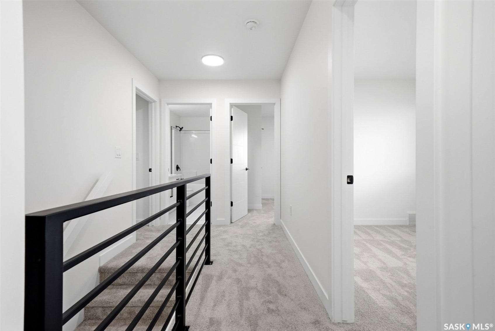 Open hallway with a modern black metal railing, gray patterned carpeting, and white walls