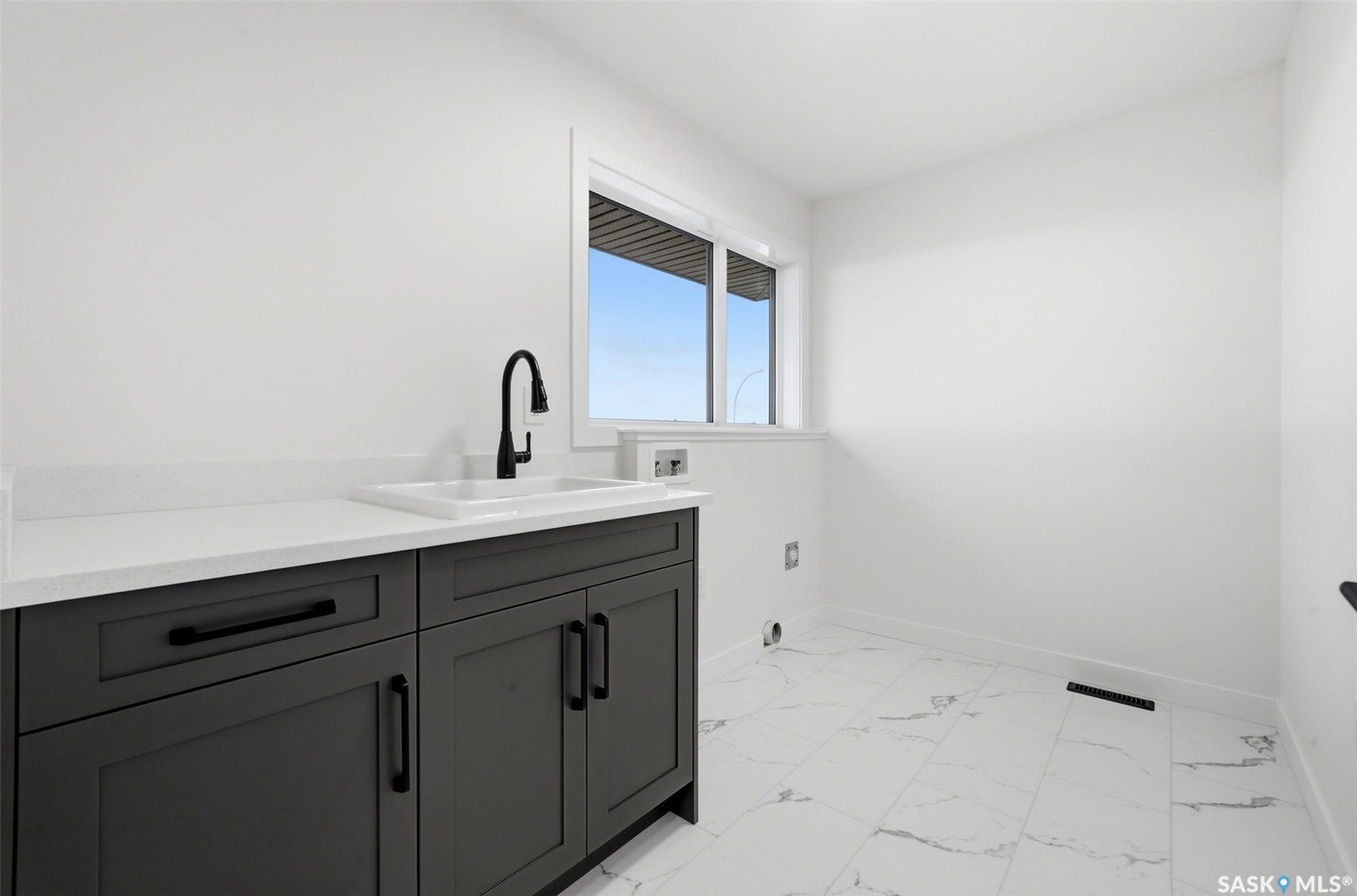 Dark wood-finish cabinetry with matte black hardware, white countertop with an integrated sink, matte black faucet, and a window providing natural illumination