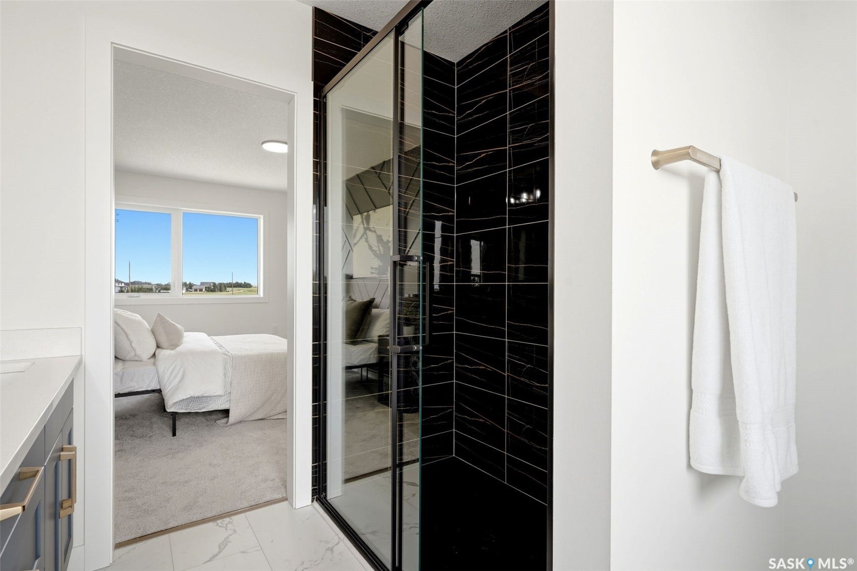Glass-enclosed shower with black tile surround, white wall paint, and a metal towel bar