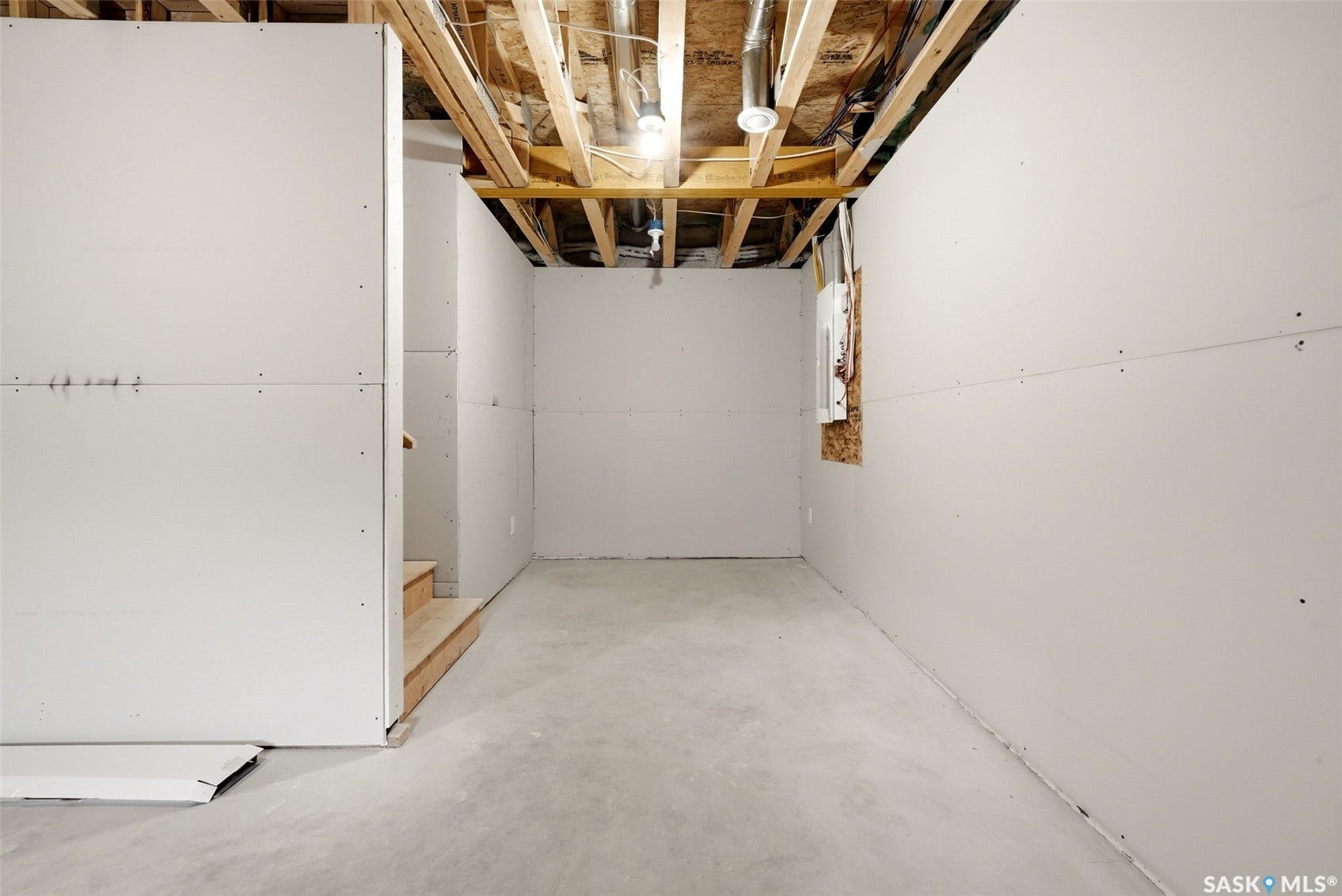 Unfinished basement space with exposed ceiling joists, partially installed drywall, and a concrete floor