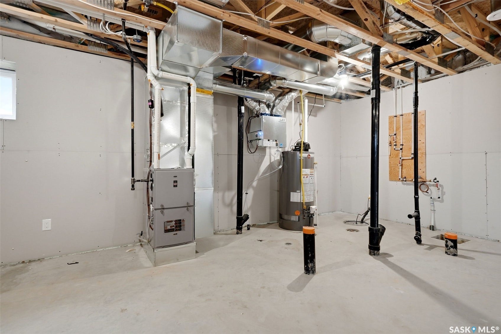 Unfinished lower level with exposed ceiling joists, concrete flooring, and a water heater