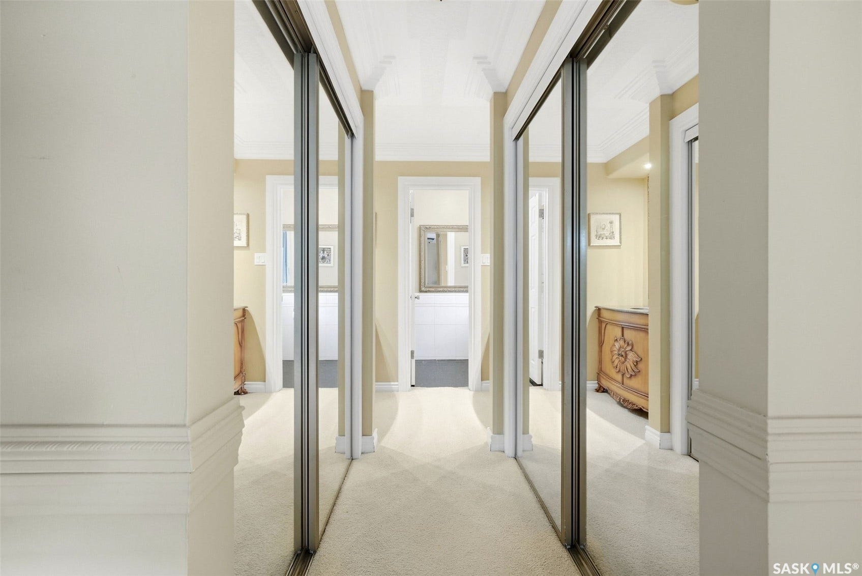 Hallway featuring mirrored sliding doors, light-toned carpeting, crown molding, and decorative wall trim