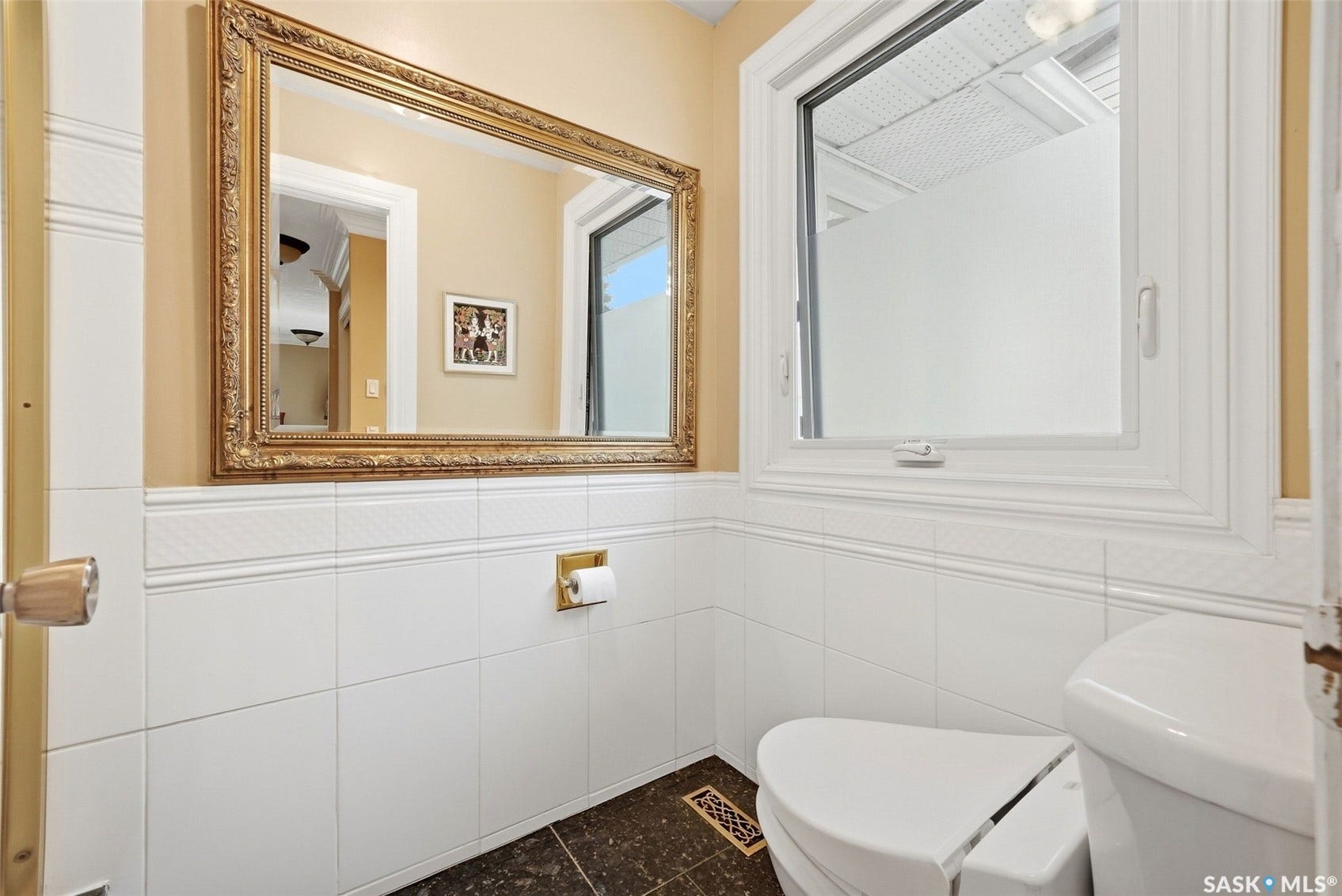 White tiled wainscoting, ornate framed mirror, and a window with white trim