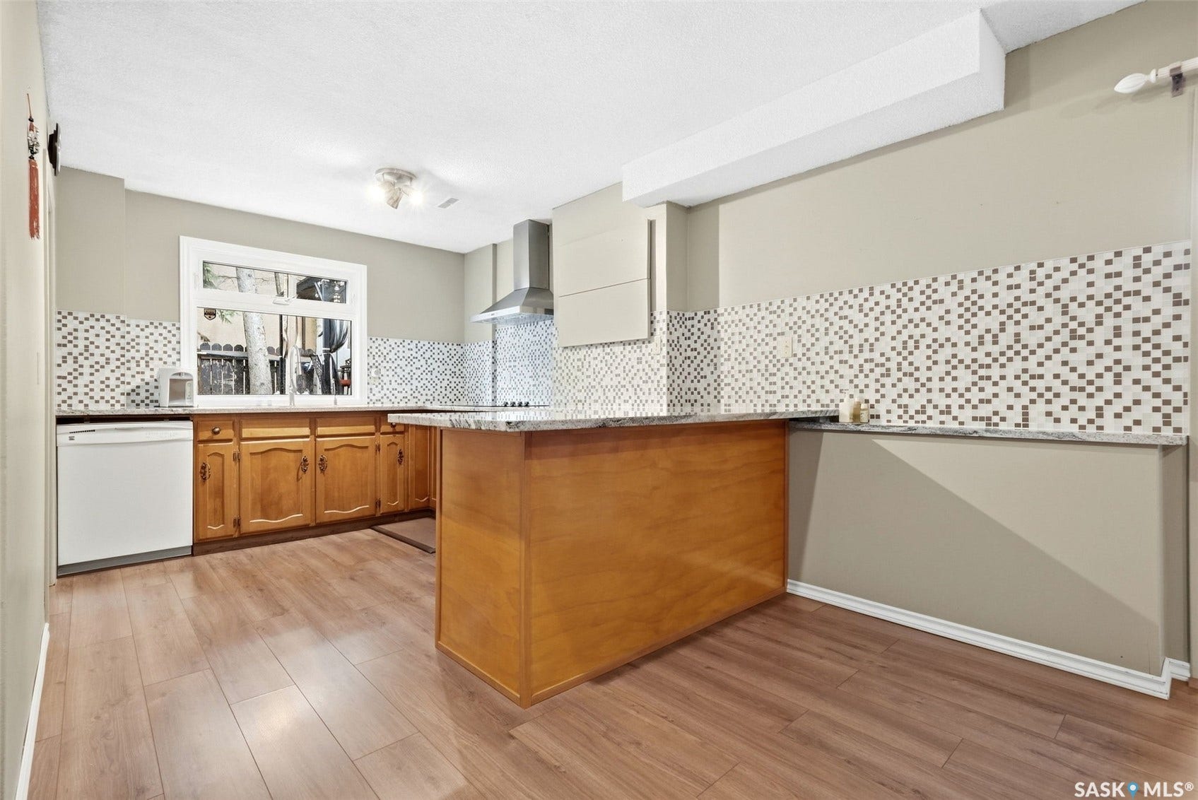 Wood-finish flooring, wood cabinetry, mosaic tile backsplash, granite countertops, and stainless steel range hood