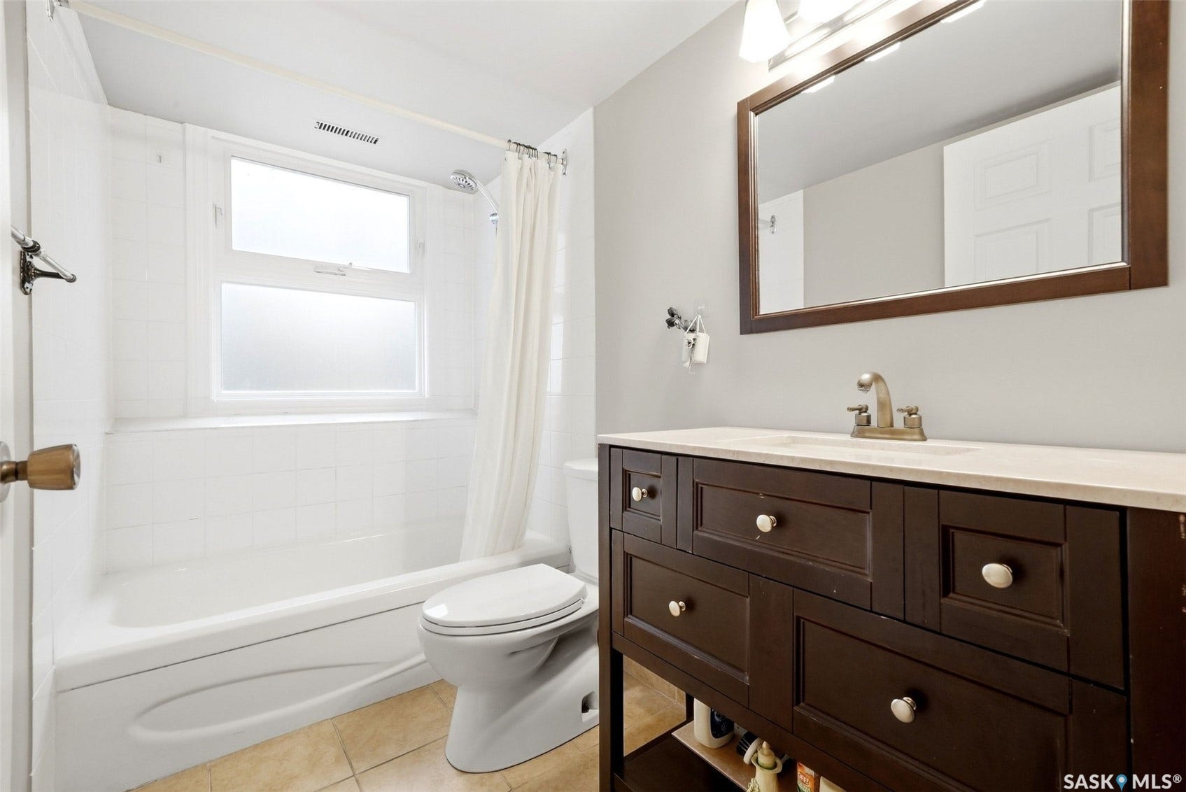 Bathroom featuring a vanity with a light-toned countertop, framed mirror, wall-mounted light fixture, tile flooring, and a bathtub with tiled surround