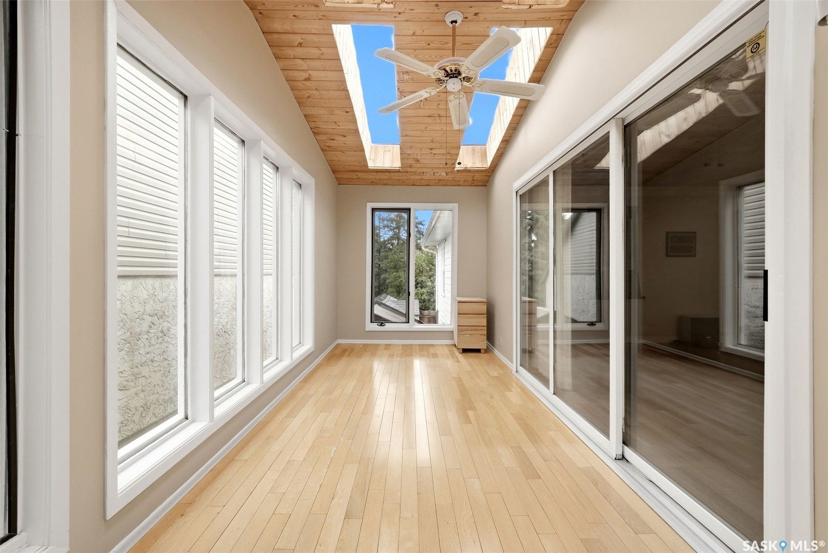 Wood-finish flooring, wood-paneled ceiling, multiple skylights, ceiling fan, and sliding glass doors