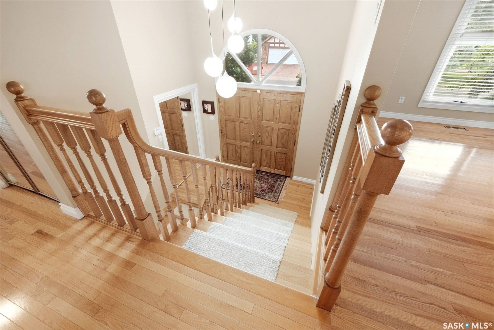 Hardwood flooring, wood staircase with balusters, wood paneled double entry doors, transom window, and a spherical pendant light fixture