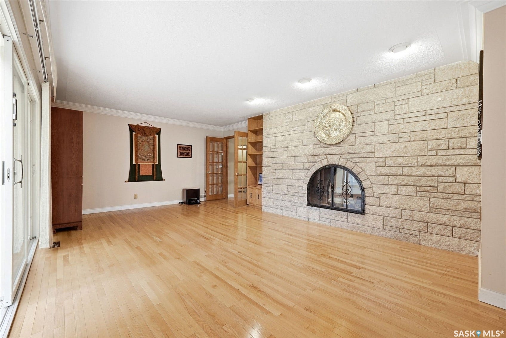 Stone-clad fireplace with an arched firebox, wood-finish flooring, built-in shelving, and sliding glass doors
