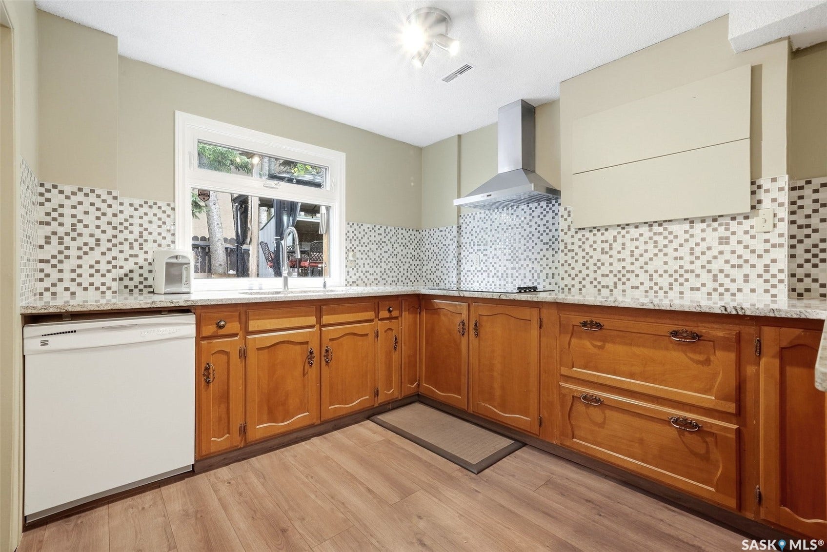 Kitchen featuring wood-finish flooring, wood cabinetry with decorative hardware, a mosaic tile backsplash, and a stainless steel range hood