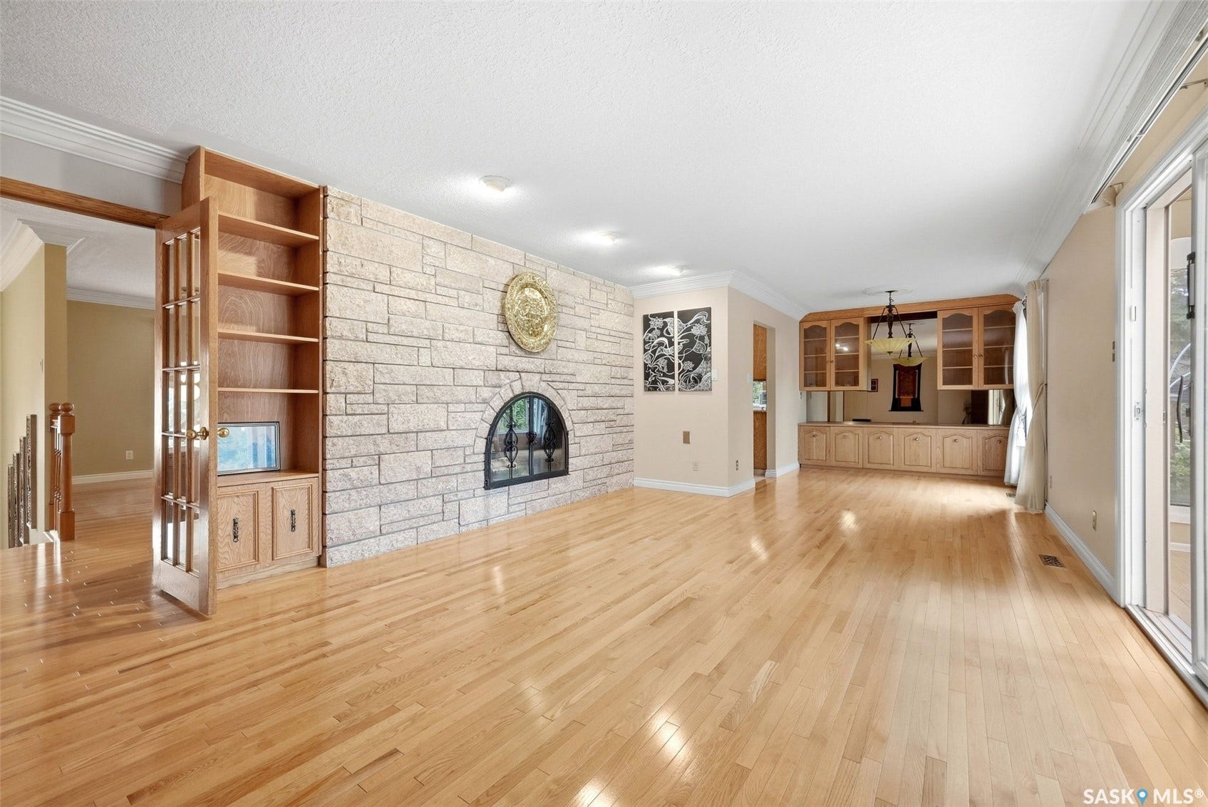 Hardwood flooring, a stone-faced fireplace, built-in shelving, built-in cabinetry with glass doors, and sliding patio doors