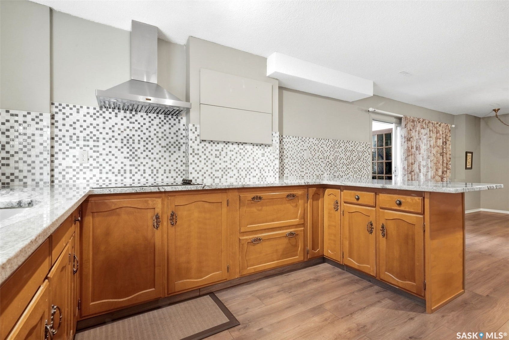 U-shaped kitchen featuring light wood cabinetry, stone countertops, mosaic tile backsplash, and a stainless steel range hood