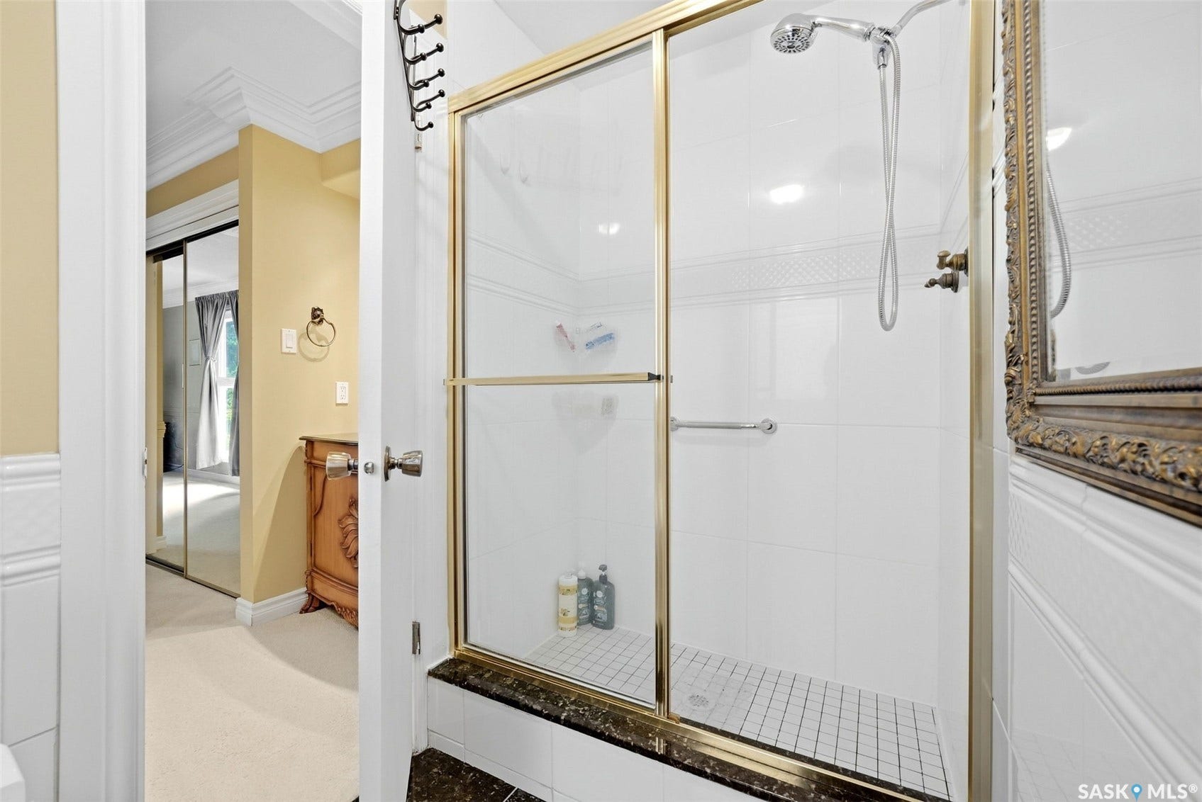 Shower enclosure with gold-finish framing, white subway tile surround, and a coordinating mosaic tile floor