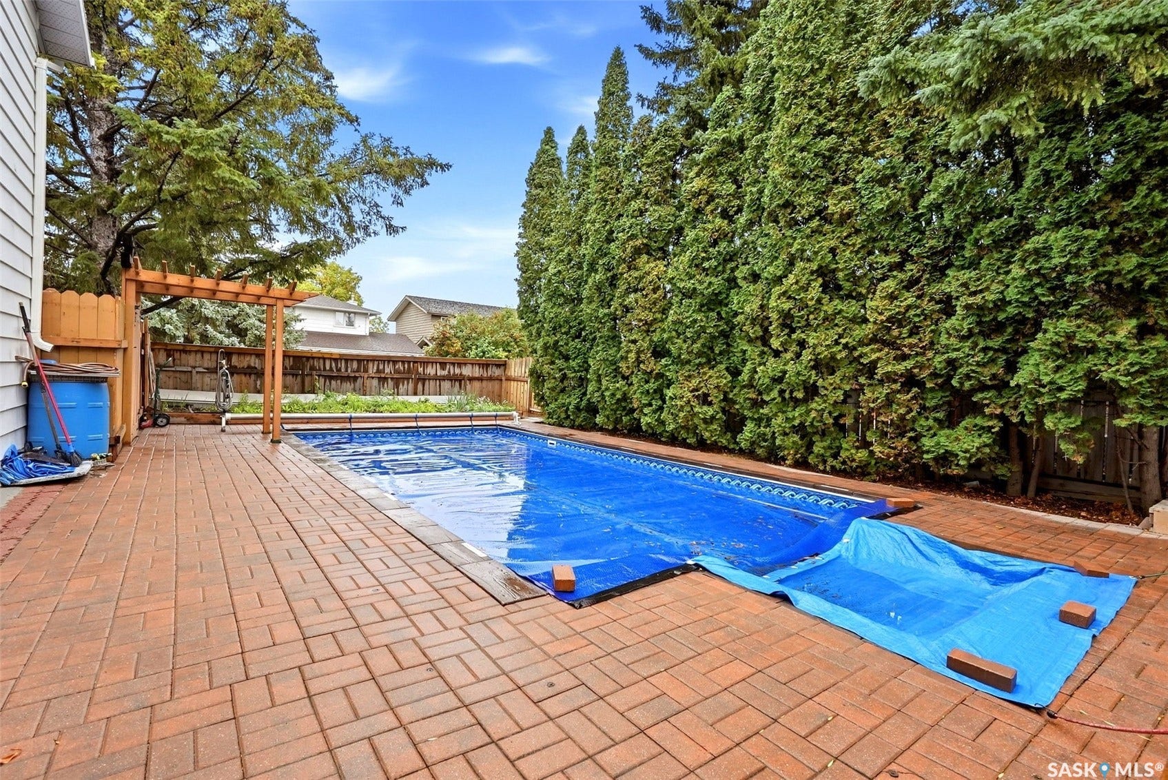 In-ground swimming pool with a brick paver patio, wood privacy fence, and mature evergreen perimeter landscaping
