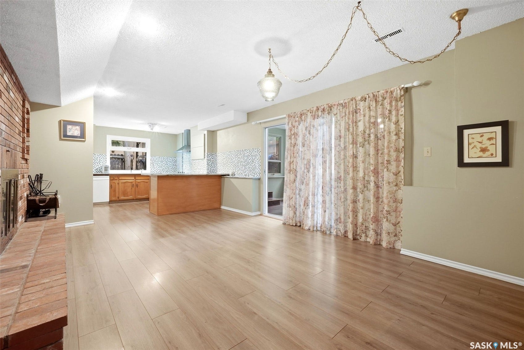 Brick fireplace, light wood-finish flooring, sliding glass door, recessed lighting, and kitchen area with wood cabinetry