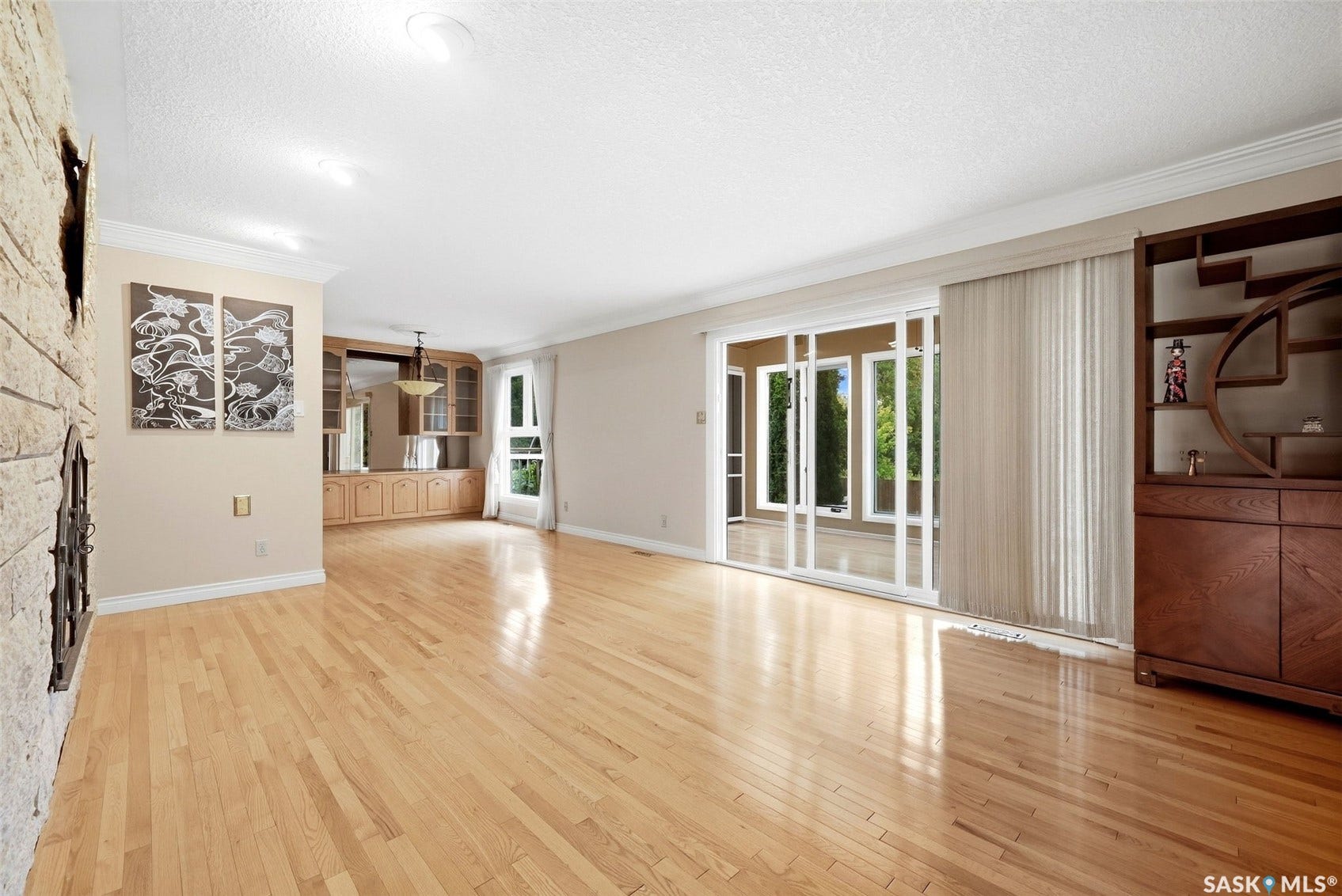 Hardwood flooring throughout, stone-clad fireplace, built-in wooden cabinetry with mirrored accents, and sliding glass patio doors