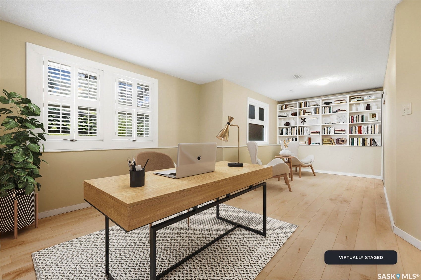 Light wood-finish flooring, two large windows with white louvered shutters, and a wall of built-in shelving