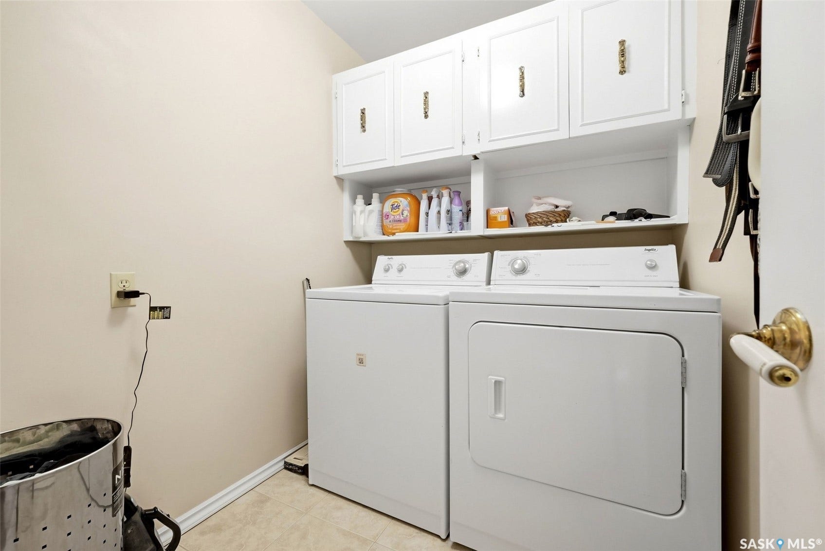 Laundry area featuring upper cabinetry with brass-toned hardware, open shelving, and light-toned flooring
