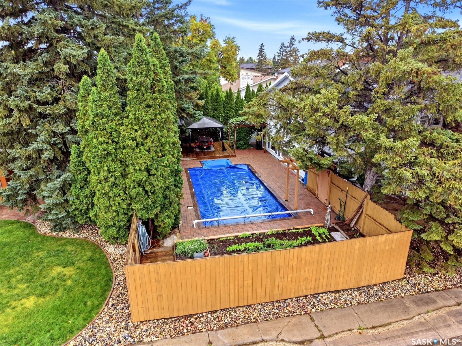 In-ground swimming pool with a covered surface, brick paver surround, and adjacent wooden pergola