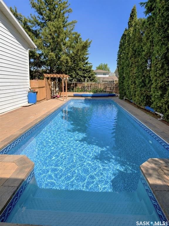 In-ground swimming pool with integrated steps, paver surround, and wood pergola