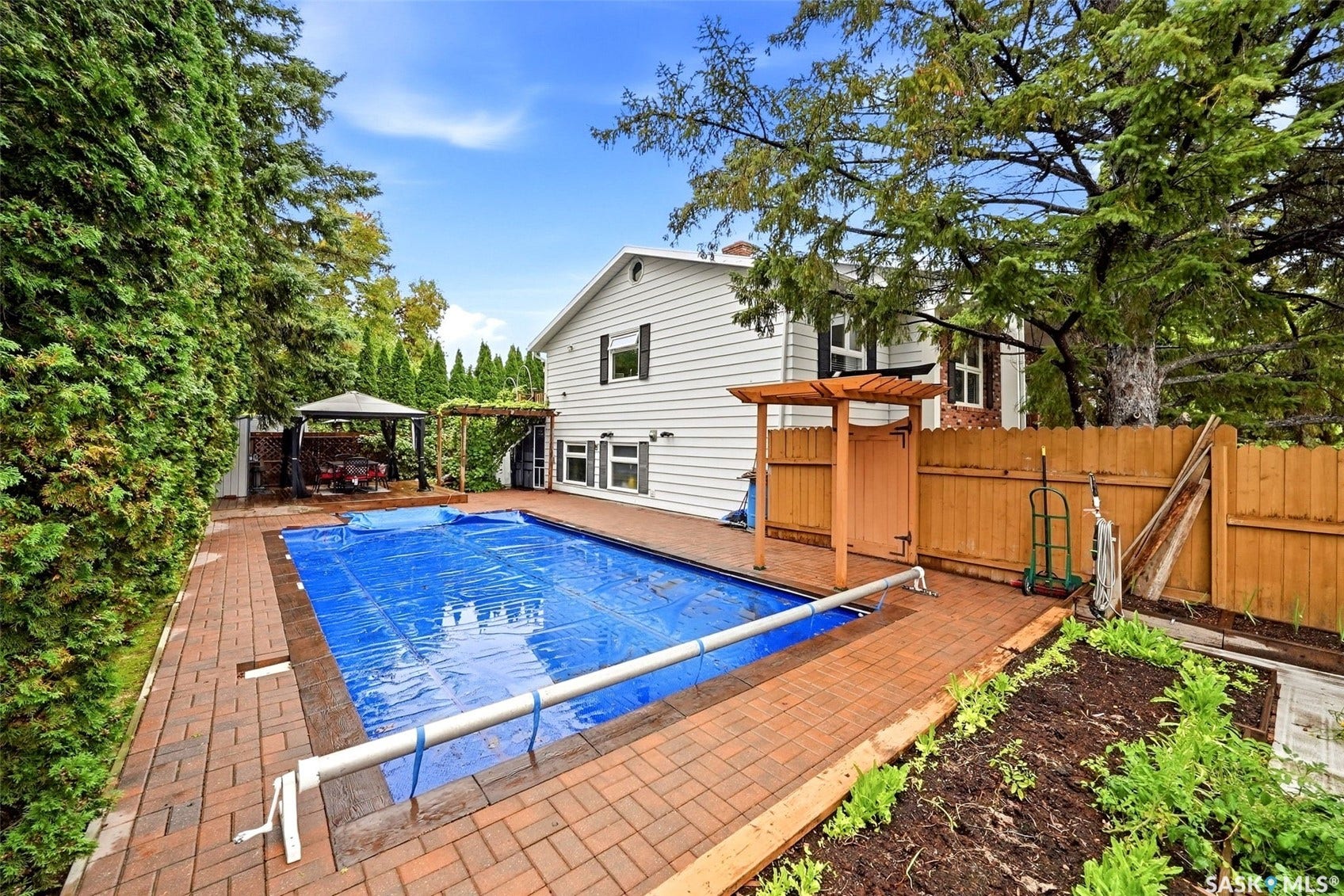 Backyard featuring a covered swimming pool, brick paver patio, wood gazebo, and a privacy fence