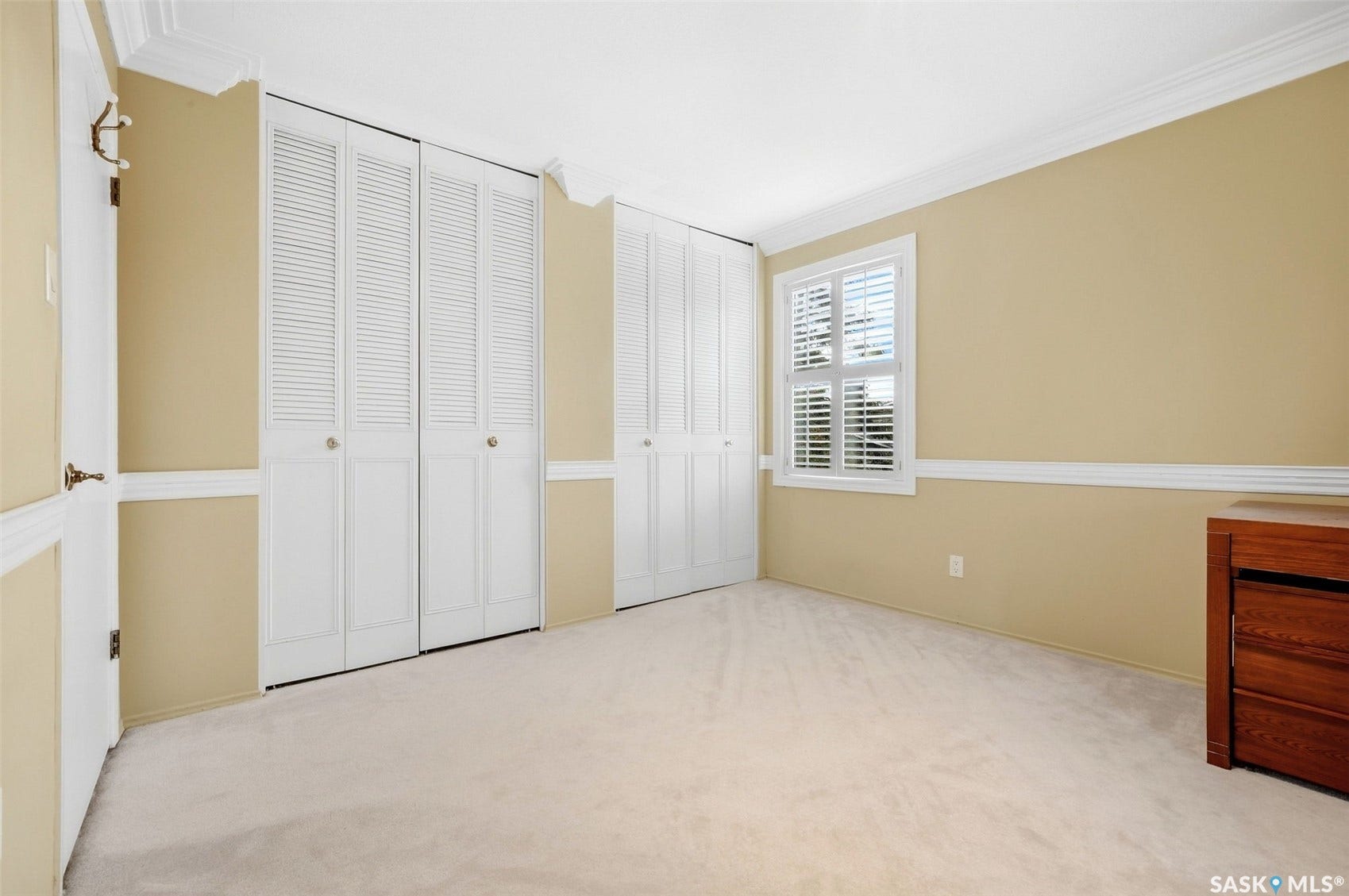 Plush carpeting, crown molding, chair rail molding, white louvered bifold closet doors, and white plantation shutters on the window