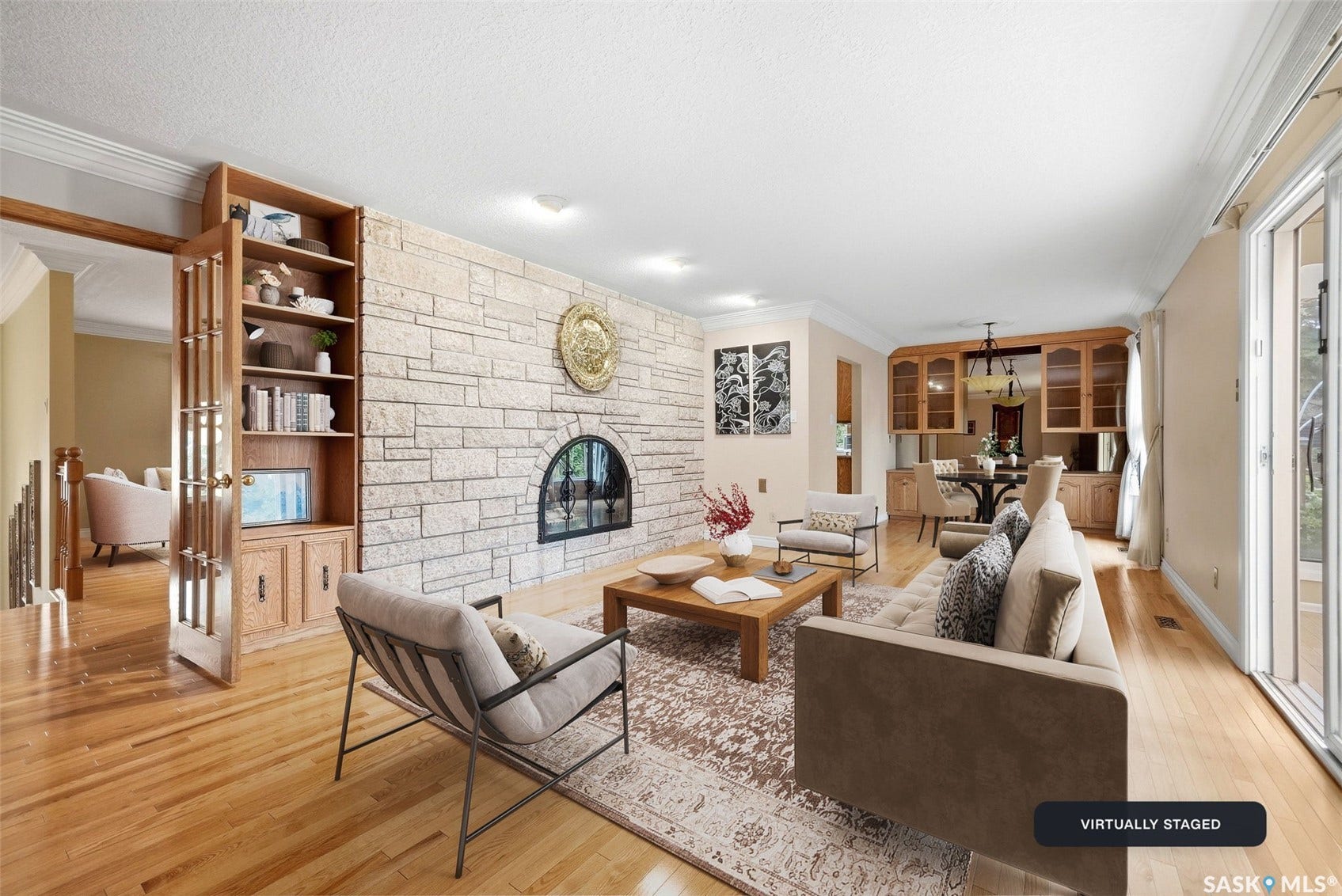 Living area with wood-finish flooring, a stone-clad fireplace, built-in shelving, crown molding, and sliding glass doors