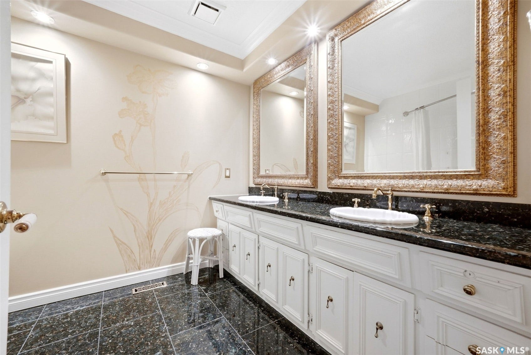 Double vanity with white cabinetry, dark speckled countertop, and two ornate framed mirrors