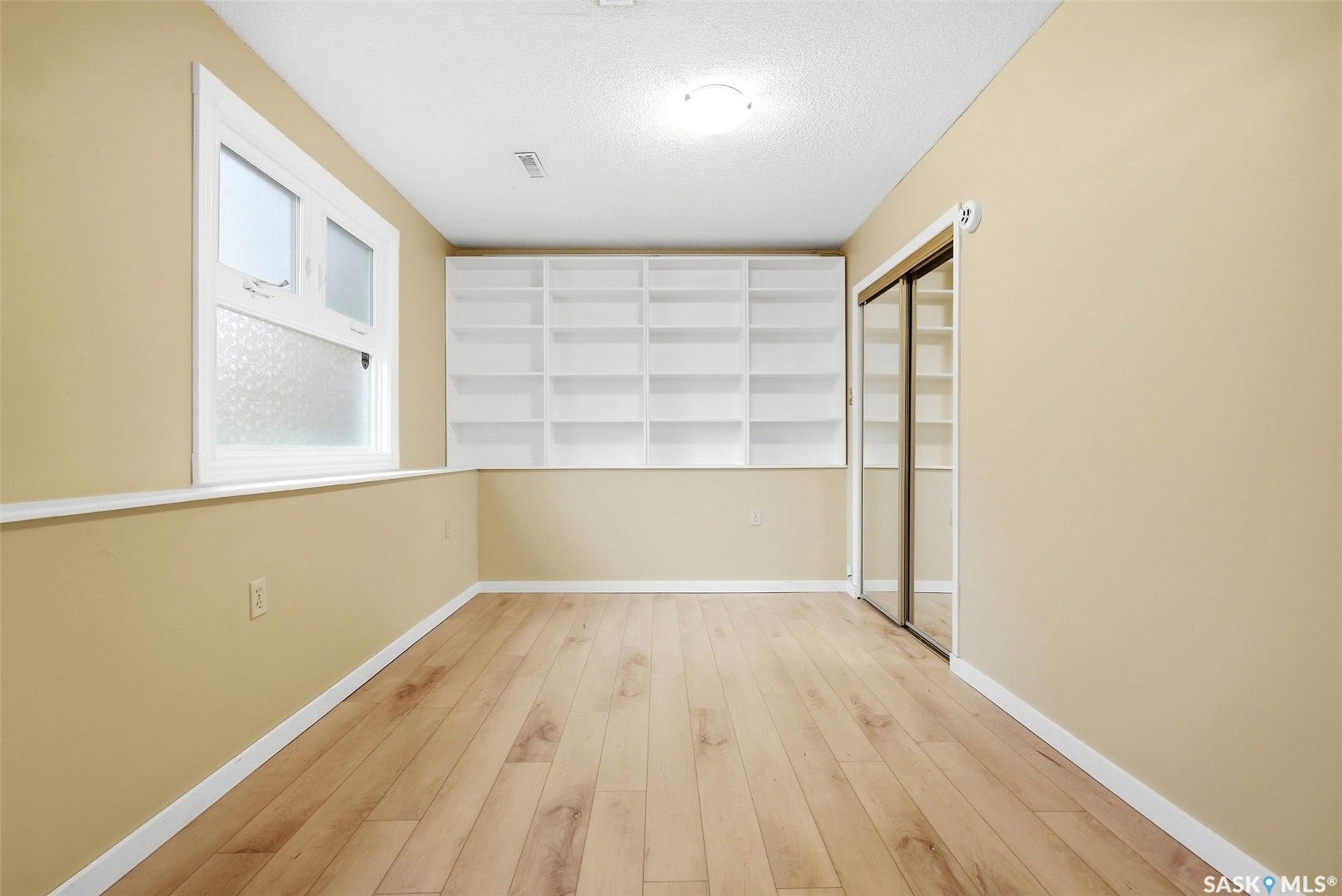 Wood-finish flooring, built-in shelving, white trim, window, and mirrored closet doors