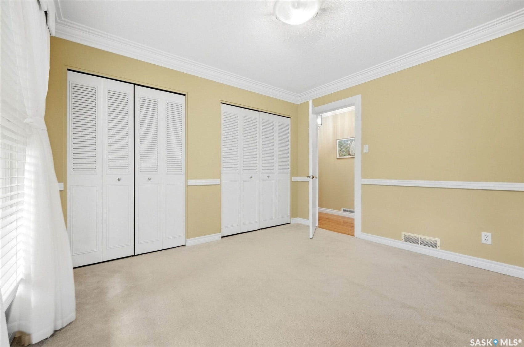 Dual louvered bi-fold closets, crown molding, chair rail molding, wall-to-wall carpeting, and an overhead lighting fixture