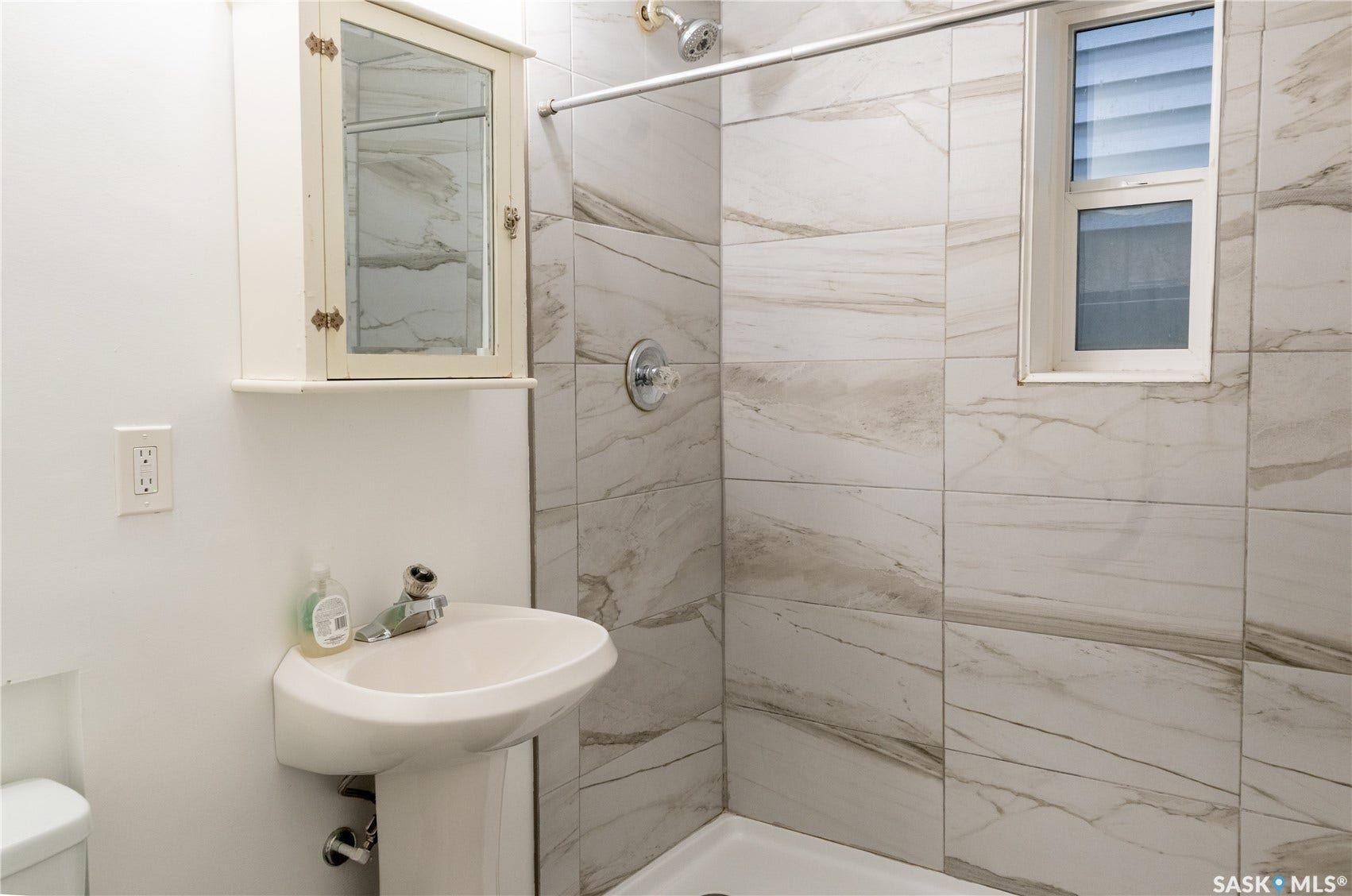 2232 McAra Street, Regina SK S4N 2W1 Pedestal sink with chrome faucet, wall-mounted medicine cabinet, shower with large format tile surround, and an integrated shower window
