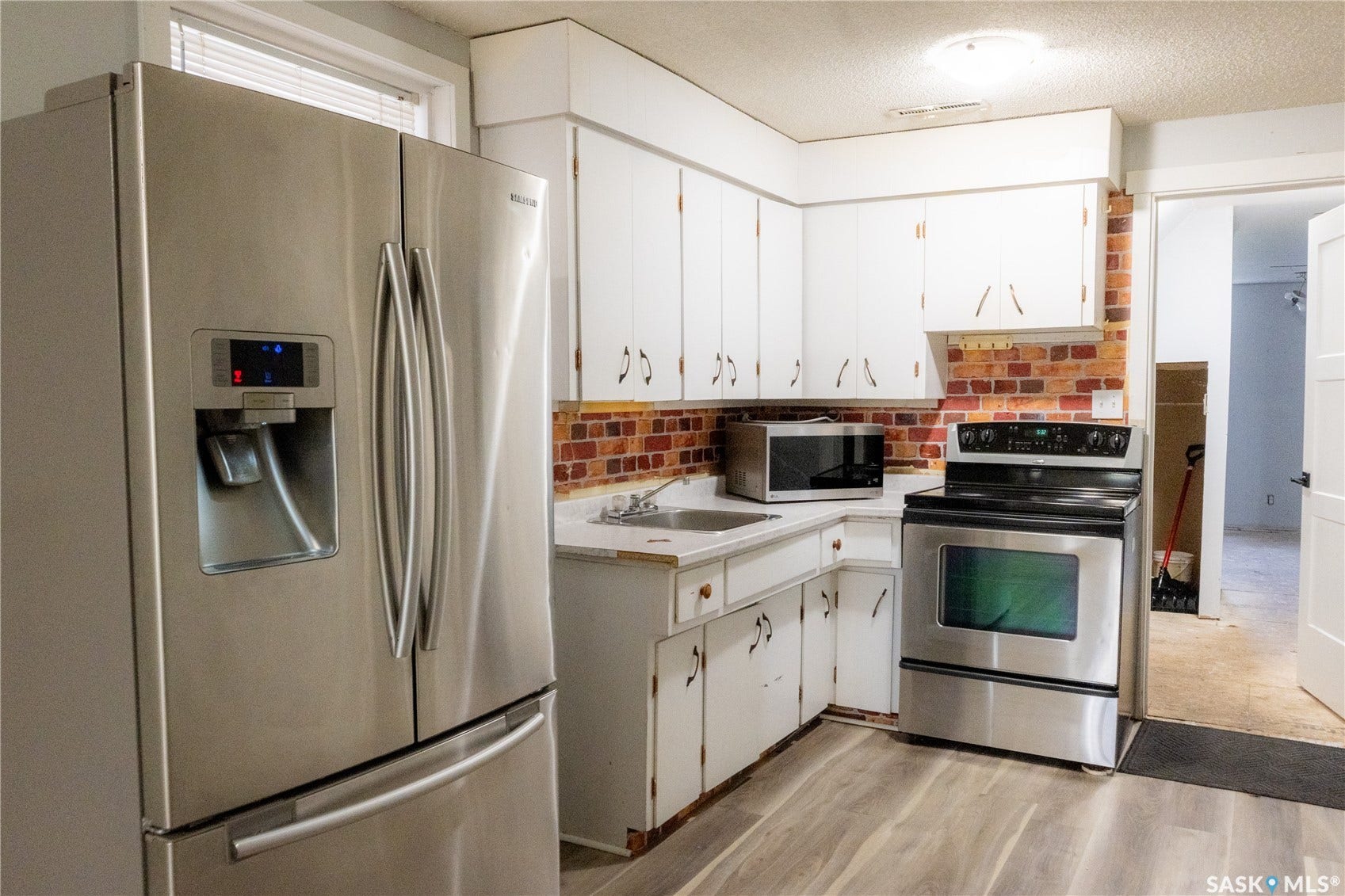 2232 McAra Street, Regina SK S4N 2W1 Kitchen featuring white cabinetry, wood-finish flooring, and a brick-patterned backsplash