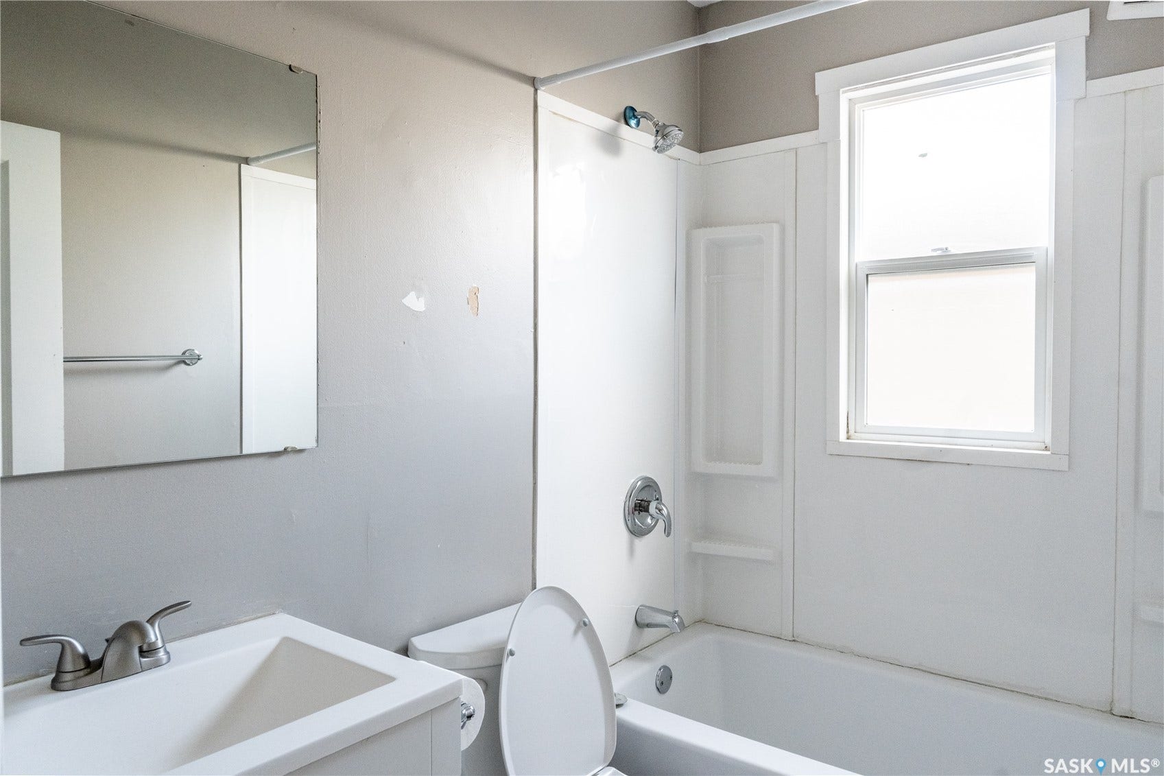 2232 McAra Street, Regina SK S4N 2W1 Single-pane window, white vanity with integrated sink, chrome faucet, wall-mounted mirror, and a white shower-over-tub combination
