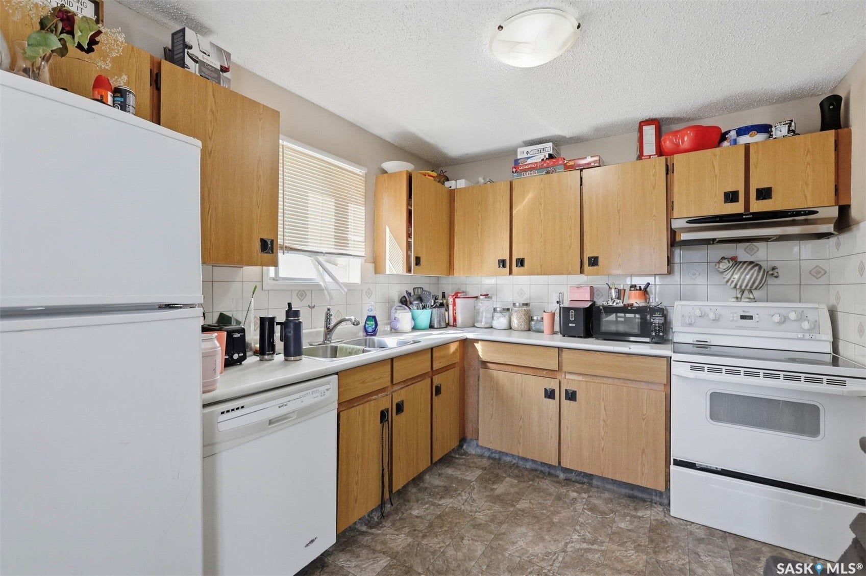 Kitchen featuring wood-finish cabinetry, white appliances, white countertops, and a tile backsplash