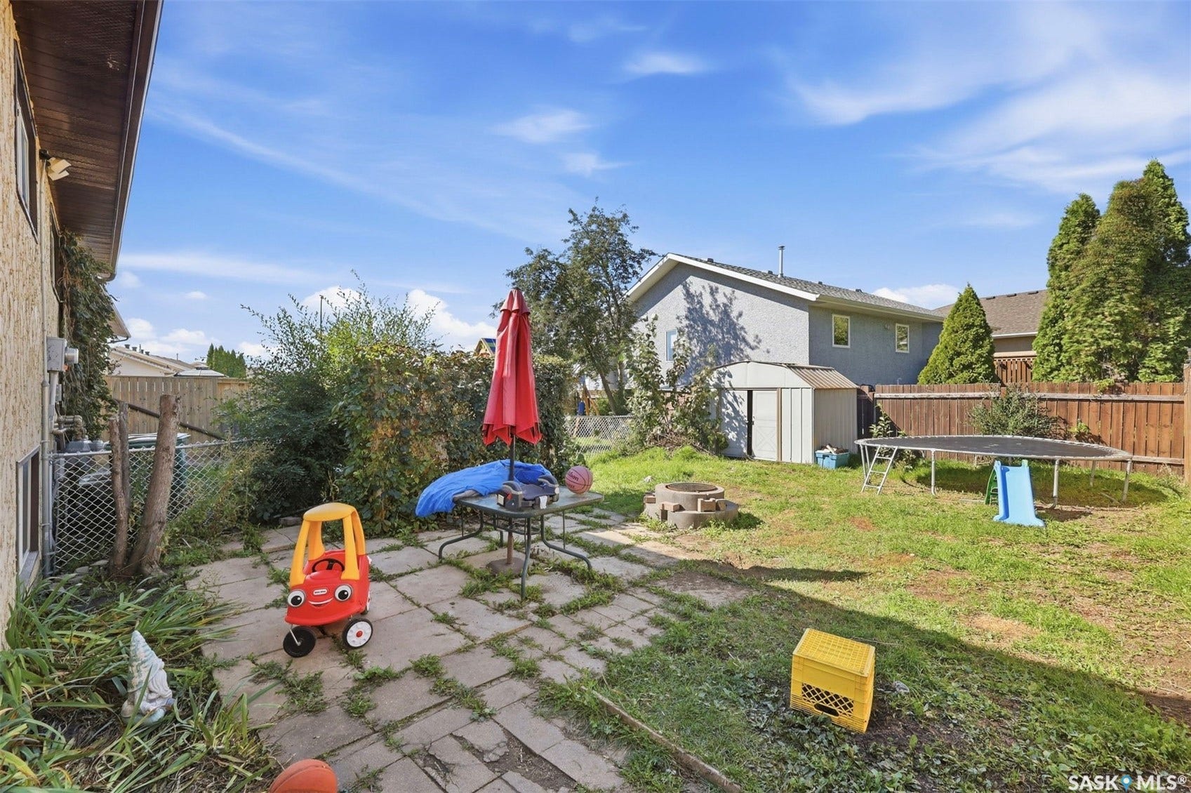 Backyard featuring a concrete paver patio, a fenced perimeter, a storage shed, and a fire pit