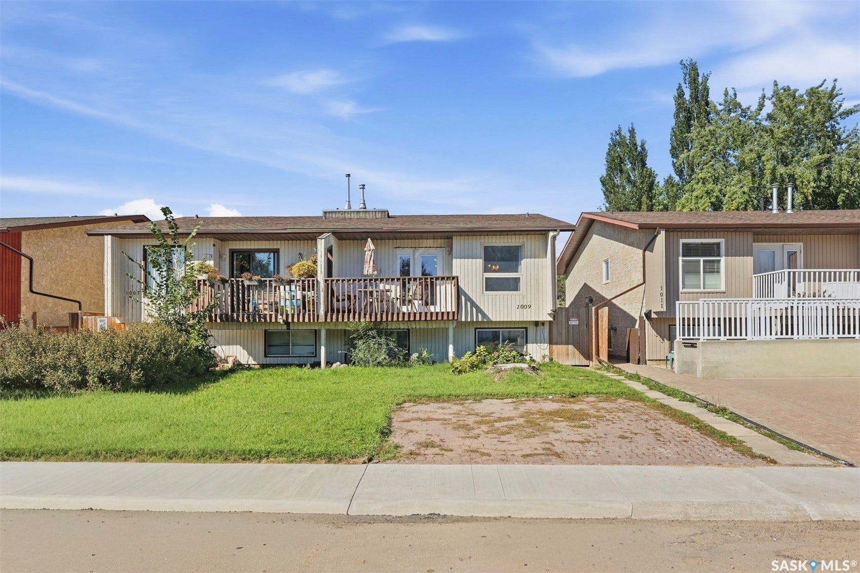 Two-story residence featuring a wood deck, upper-level balcony, and a paved driveway