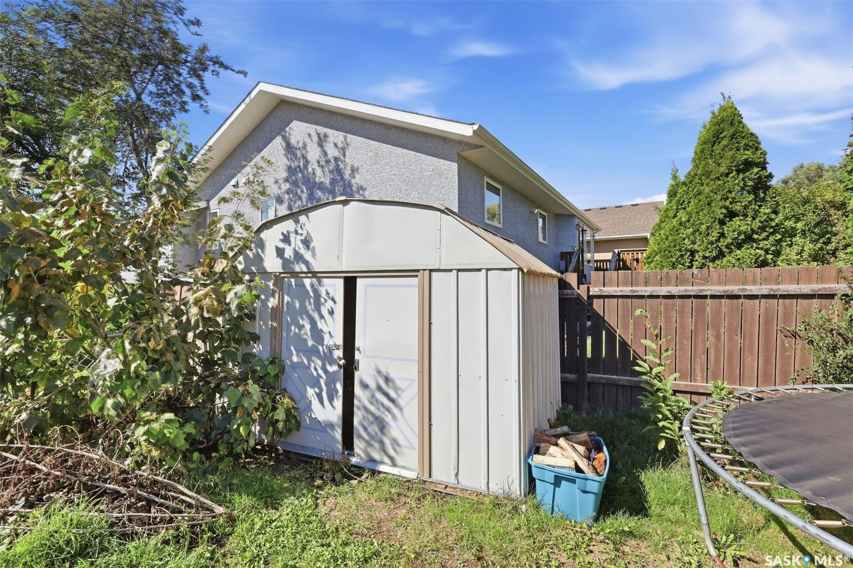 Detached storage shed with a single door, surrounded by mature perimeter trees and a wood fence