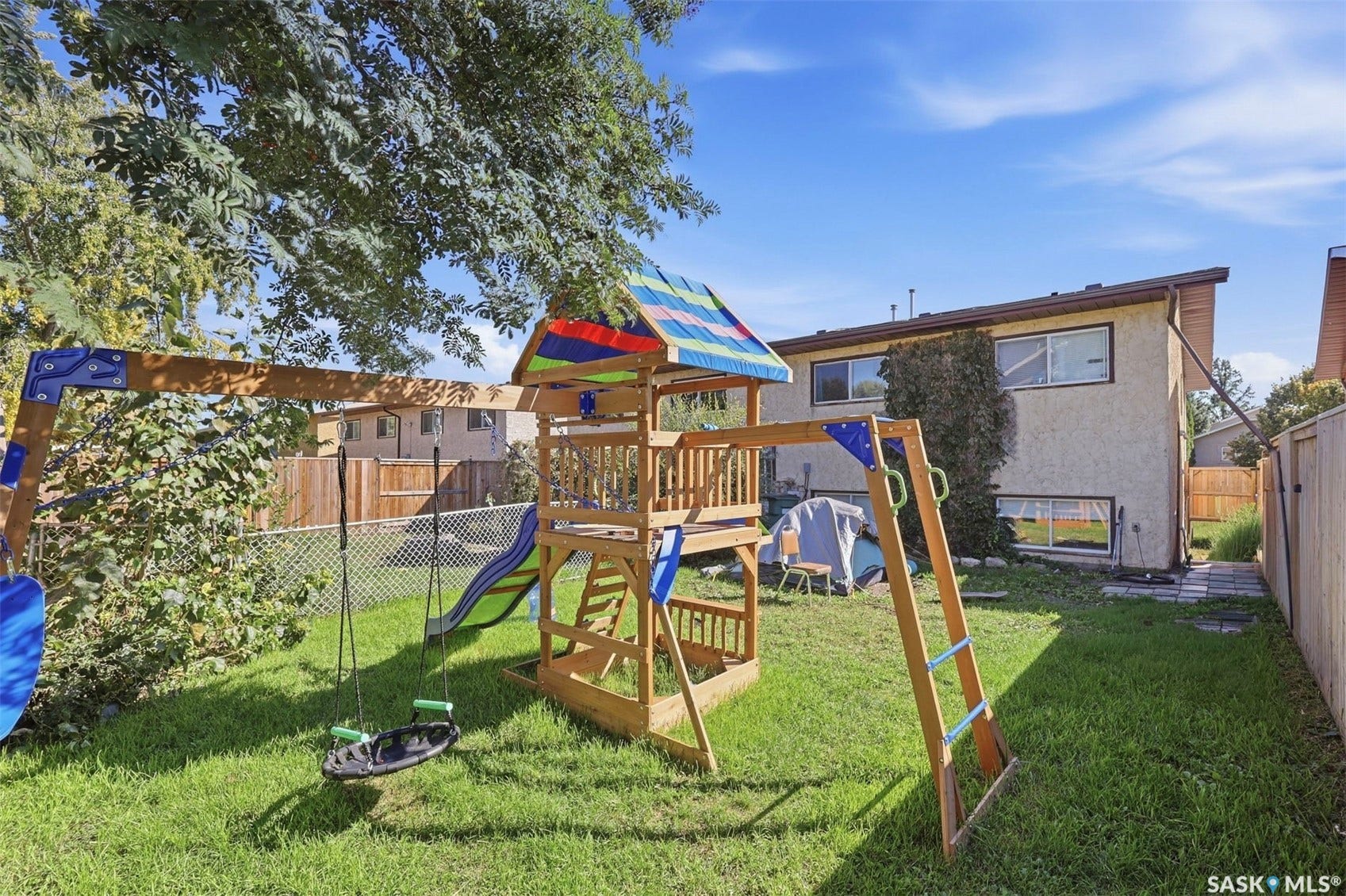 Expansive backyard featuring a manicured lawn, chain-link fence, and a wooden playground structure