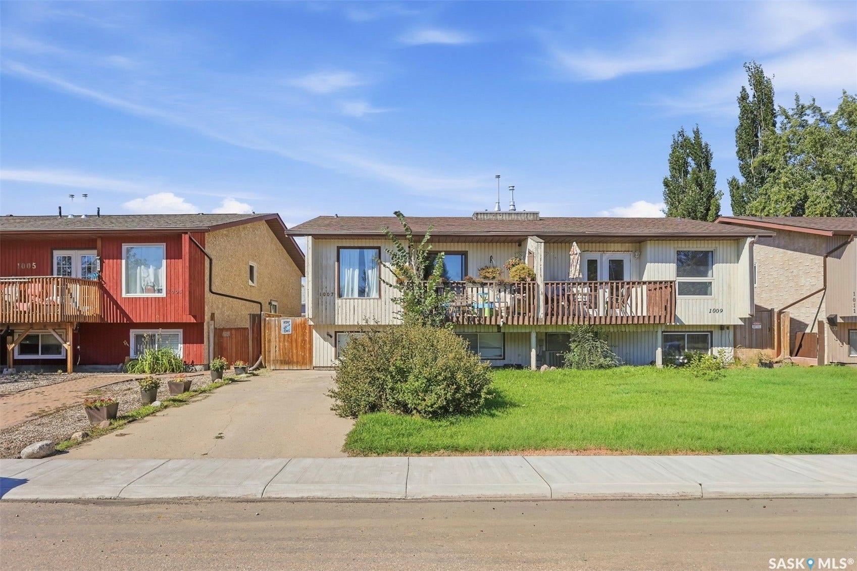 Exterior features a light-toned facade, a prominent wooden deck with railing, and a well-maintained green lawn