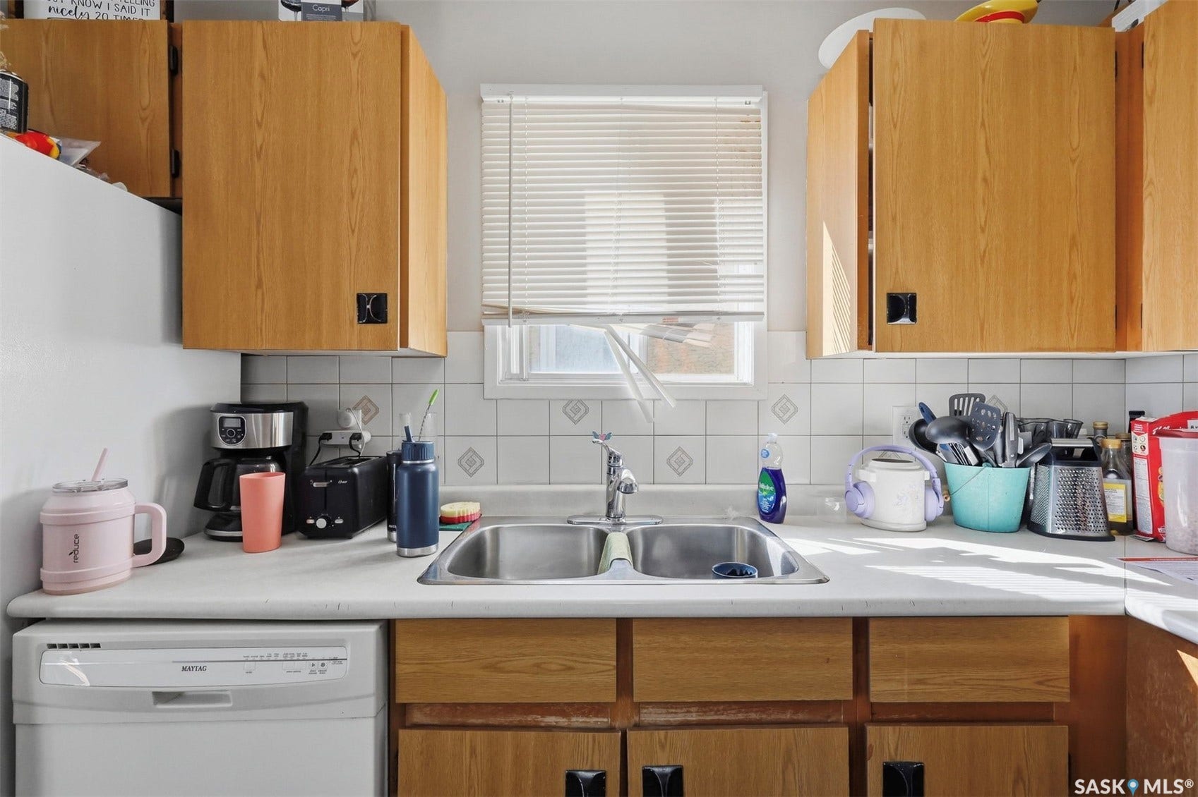 Wood-finish cabinetry, solid surface countertop, stainless steel double basin sink, and a tiled backsplash